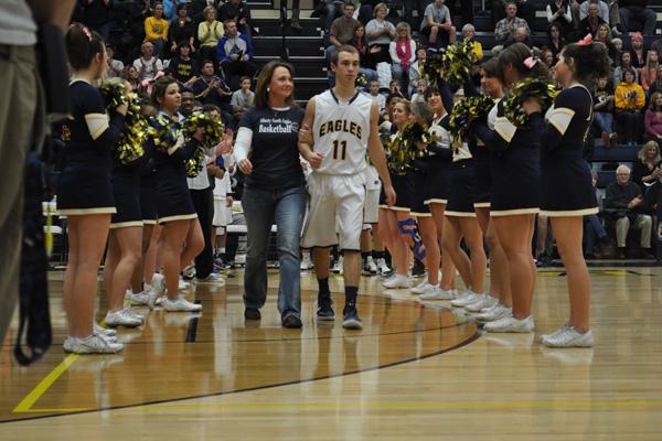 Junior Jake Hansen leads his mother and breast cancer survivor, Shelley Hansen, onto the court during the Coaches vs. Cancer game